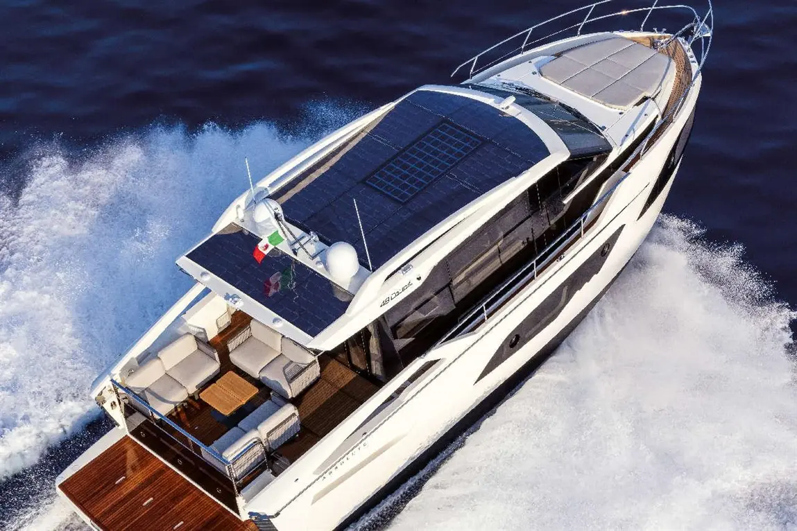 Luxury motor yacht with solar panels speeding through water, featuring a spacious deck with seating and a wooden floor.